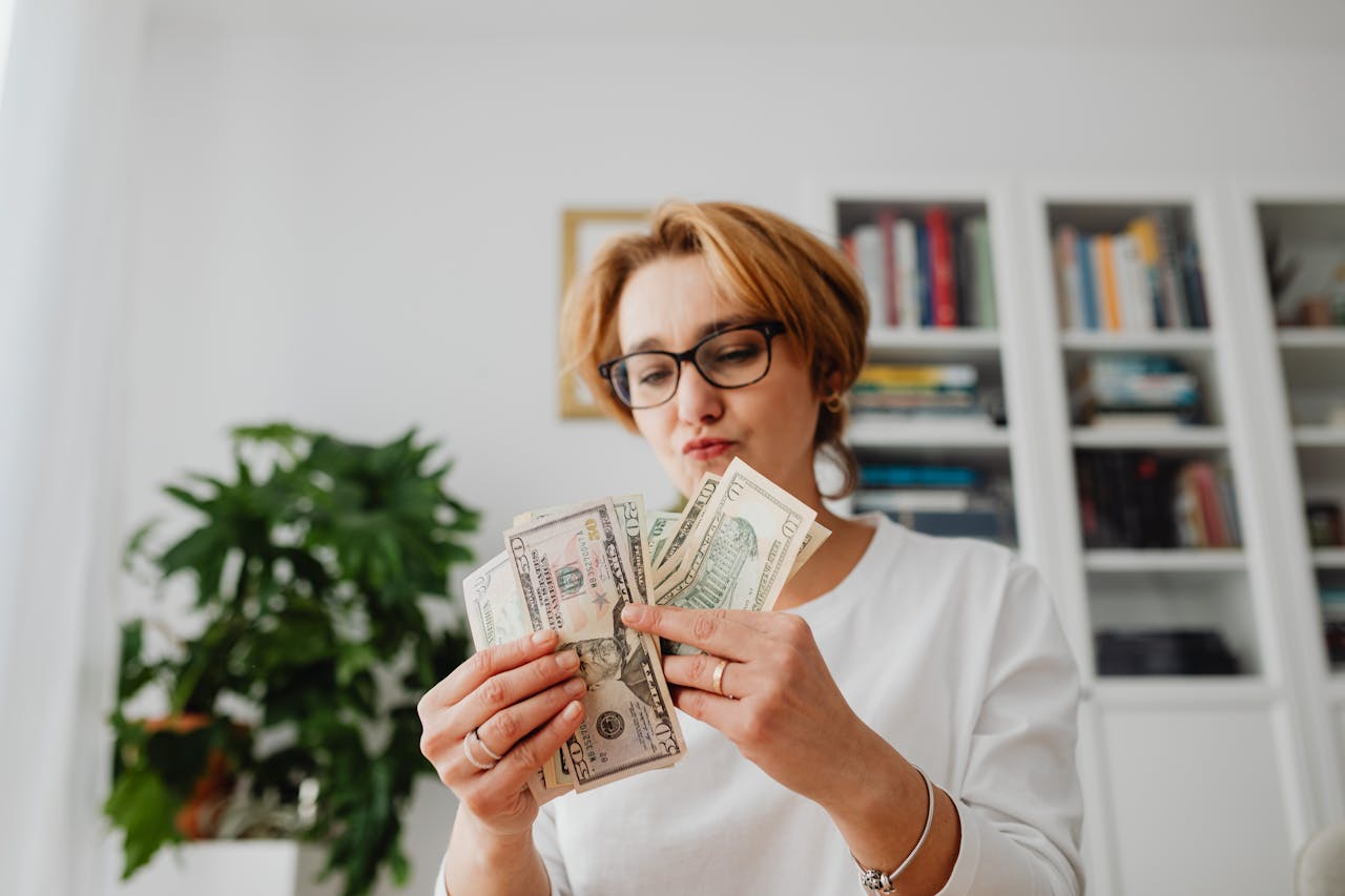 Woman with eyeglasses counting dollar bills in a home setting